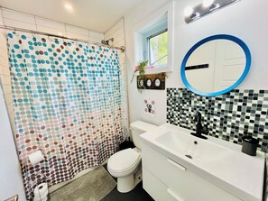 A bathroom with a white toilet, a white sink with a black faucet, a blue-framed mirror, and a shower curtain with a polka dot pattern.