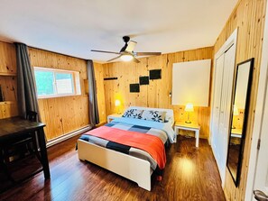 A room with a bed, two bedside tables with lamps, a ceiling fan, a window with curtains, and wooden walls.