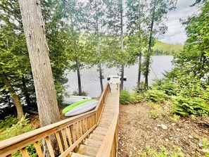 Eine Holzterrasse führt zu einem Steg über einem ruhigen See, umgeben von dichtem Wald.