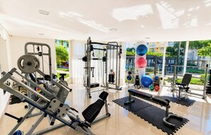 Een fitnessruimte met diverse trainingsapparaten, een bankje en uitzicht op een groen gebied buiten.