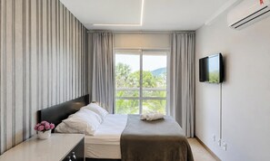 Une chambre d ’hôtel avec un lit, un téléviseur fixé au mur et une fenêtre donnant sur un paysage verdoyant.