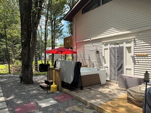 A covered outdoor area with a hot tub, a red umbrella, and a wooden deck. - +Champagne Toasts & Hot Tub Nights! Your New Abode Awaits+ NEW BEAUTIFUL HOT TUB (Tobyhanna)
