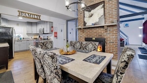 Une cuisine moderne avec des meubles blancs, un coin repas avec des chaises à motifs et une cheminée.