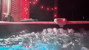 Un bain à remous doté de jets d’eau, entouré d’un éclairage d’ambiance rouge et d’une guirlande de petites lumières rouges.