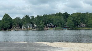 Une propriété au bord du lac, dotée d’une plage de sable, d’un quai avec des bateaux, et de maisons entourées d’arbres.