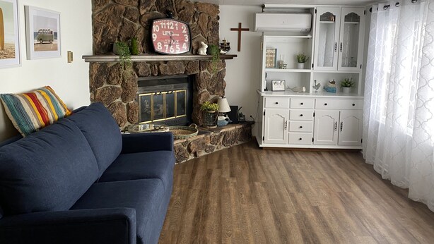 A living room with a stone fireplace, a blue sofa, a white cabinet with glass doors, and a cross on the wall. - Relax & Enjoy the Beautiful Sunsets on Lake Minnewaska.  (Starbuck)