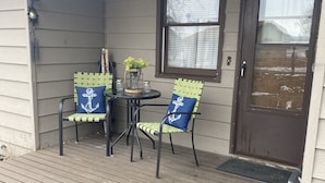 A covered porch with two chairs and a table, a door with a 'Welcome' mat, and a window with a view of a snowy landscape. - Relax & Enjoy the Beautiful Sunsets on Lake Minnewaska.  (Starbuck)