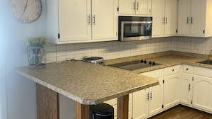 A kitchen with white cabinets, a granite countertop, a stainless steel microwave, and a wooden floor. - Relax & Enjoy the Beautiful Sunsets on Lake Minnewaska.  (Starbuck)
