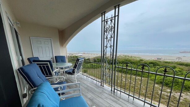 A balcony with a view of the beach, furnished with a table, chairs, and a sofa.