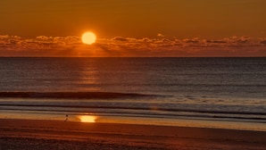 A sunset over the ocean with a beach in the foreground.
