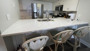 A modern kitchen with a large island, stainless steel appliances, and wicker chairs.