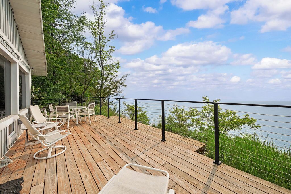 A wooden deck with lounge chairs and a table, overlooking a body of water.