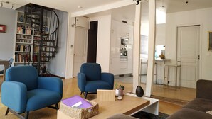 A modern living room with blue armchairs, a wooden coffee table, and a bookshelf.