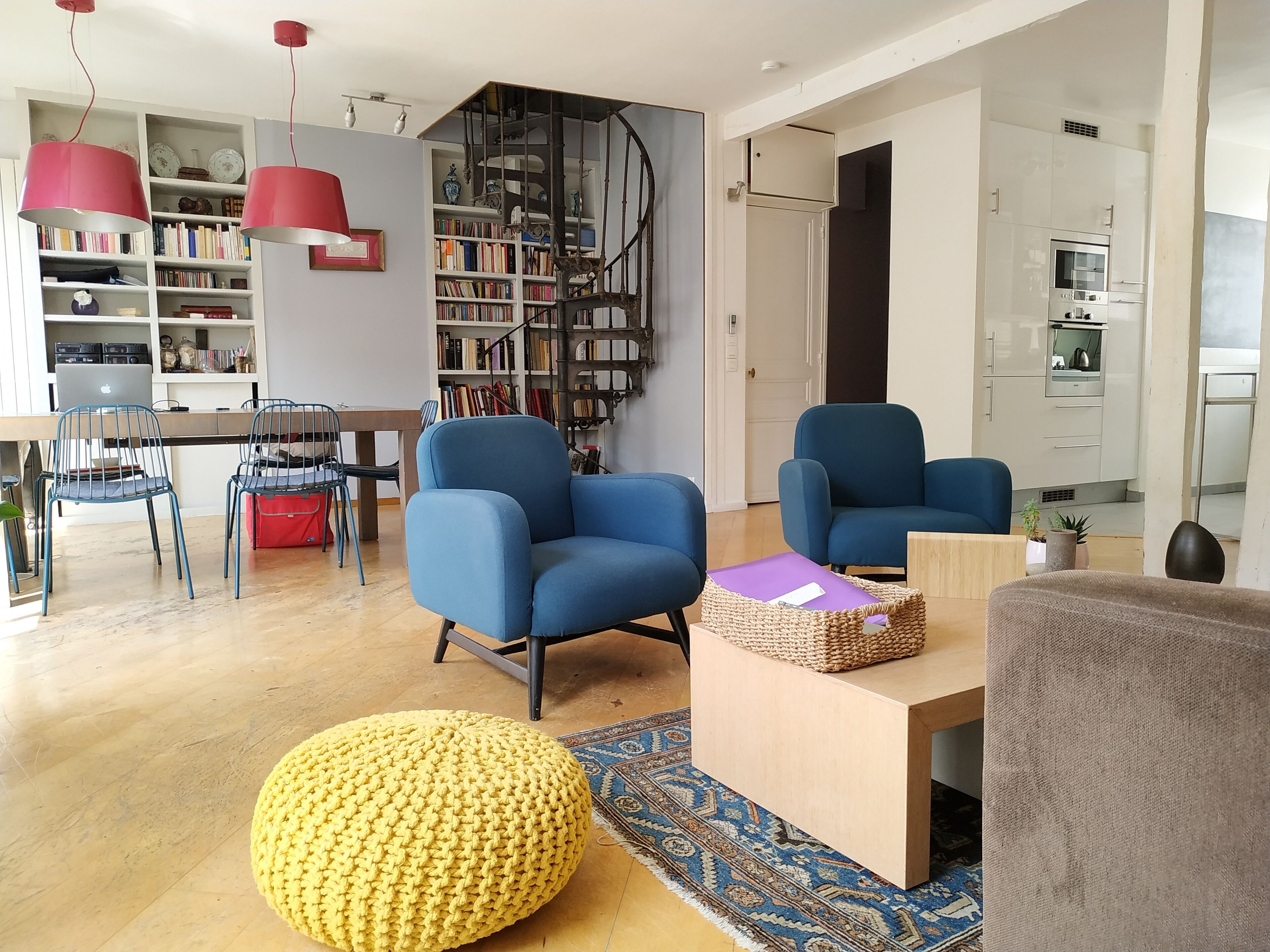 Een moderne woonkamer met blauwe fauteuils, een geel poufje en een houten salontafel.