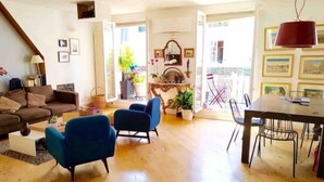 A spacious living area with a wooden floor, a brown sofa, blue armchairs, and a dining table with chairs.
