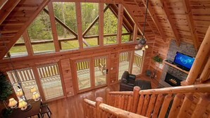 A wooden cabin interior with a dining area, seating, a fireplace, and a TV.