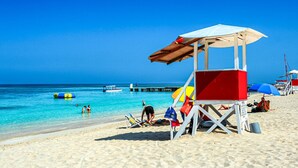 Ein Strand mit einem Rettungsturm, klarem, blauem Wasser und einem Pier im Hintergrund.
