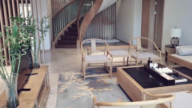 Ein modernes Wohnzimmer mit einer geschwungenen Treppe, Holzmöbeln und einem Couchtisch mit Dekorationselementen.