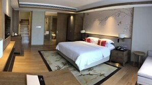 Ein Hotelzimmer mit einem großen Bett, Nachttischen, einem Schreibtisch und einem Sessel. Eine Treppe führt in einen weiteren Raum.