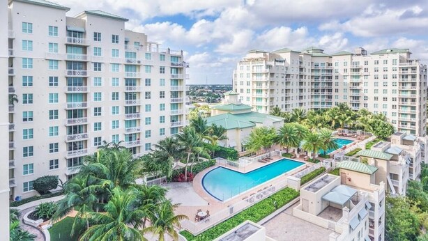 A high-rise residential building with a swimming pool surrounded by palm trees and greenery. - Serenity Ocean Luxury Condo (Boynton Beach)