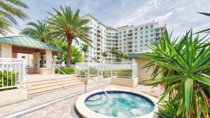 A hotel courtyard with a hot tub, palm trees, and a building with multiple balconies. - Serenity Ocean Luxury Condo (Boynton Beach)