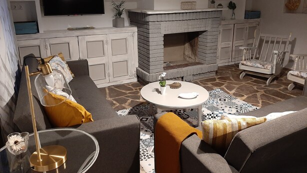 Una sala de estar con chimenea, sofá, sillón y televisor en la pared.