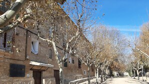 Una calle flanqueada por edificios de piedra, algunos con balcones y ventanas, bajo un cielo despejado.