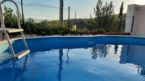 Una piscina con escalera, rodeada de vegetación y una valla.