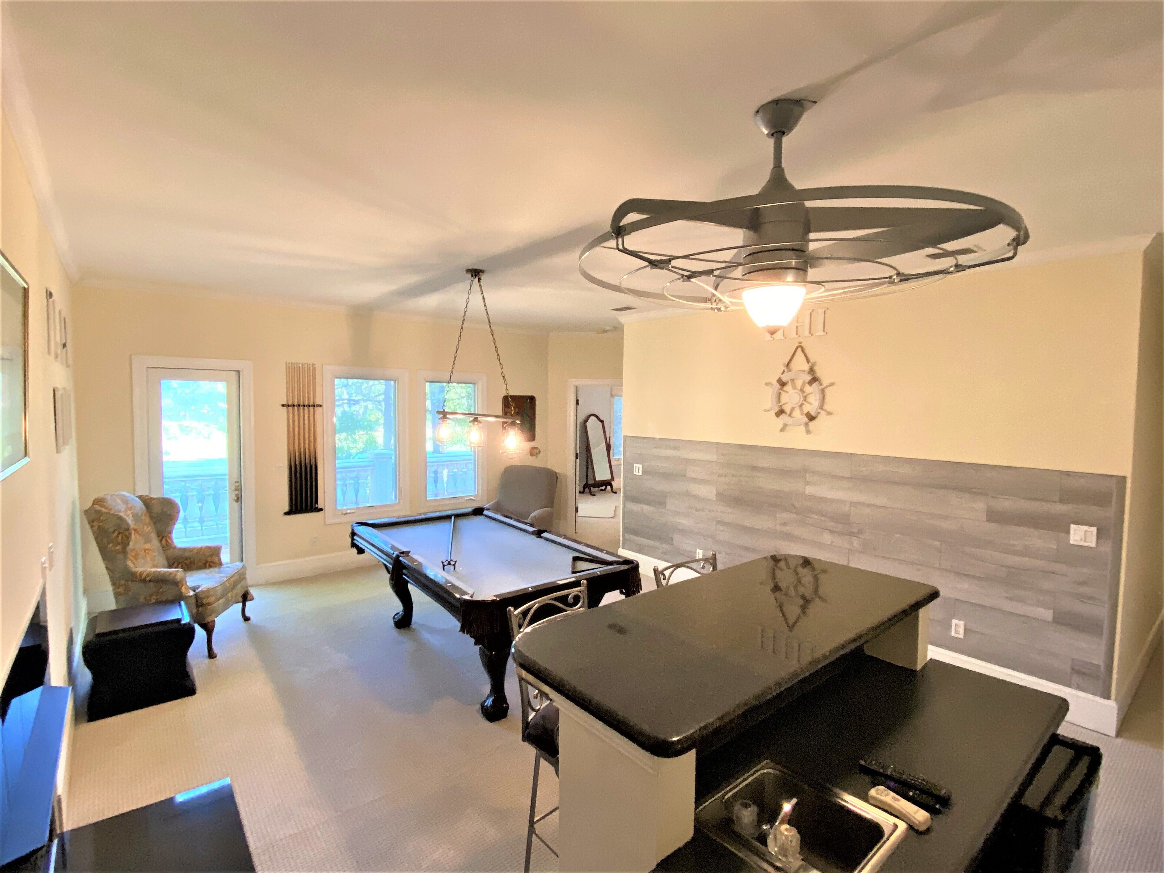 A modern kitchen with a pool table, a bar area, and a ceiling fan.