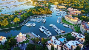 An aerial view of a marina with numerous boats docked, surrounded by lush greenery and residential buildings.