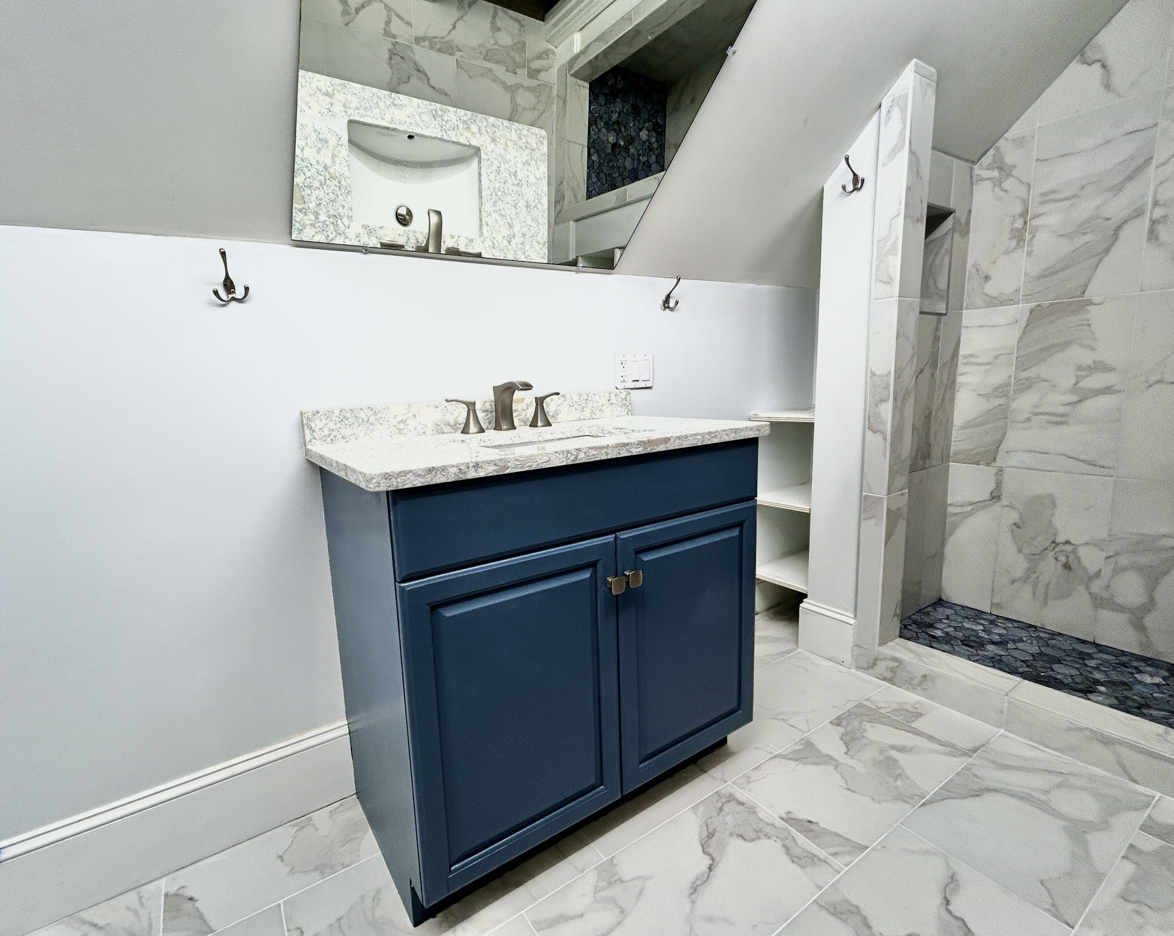 Une salle de bain avec un lavabo en marbre, des meubles de rangement bleu foncé et un espace douche.