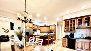 A modern kitchen with wooden cabinets, a stainless steel refrigerator, and a dining area with a glass table and white chairs.