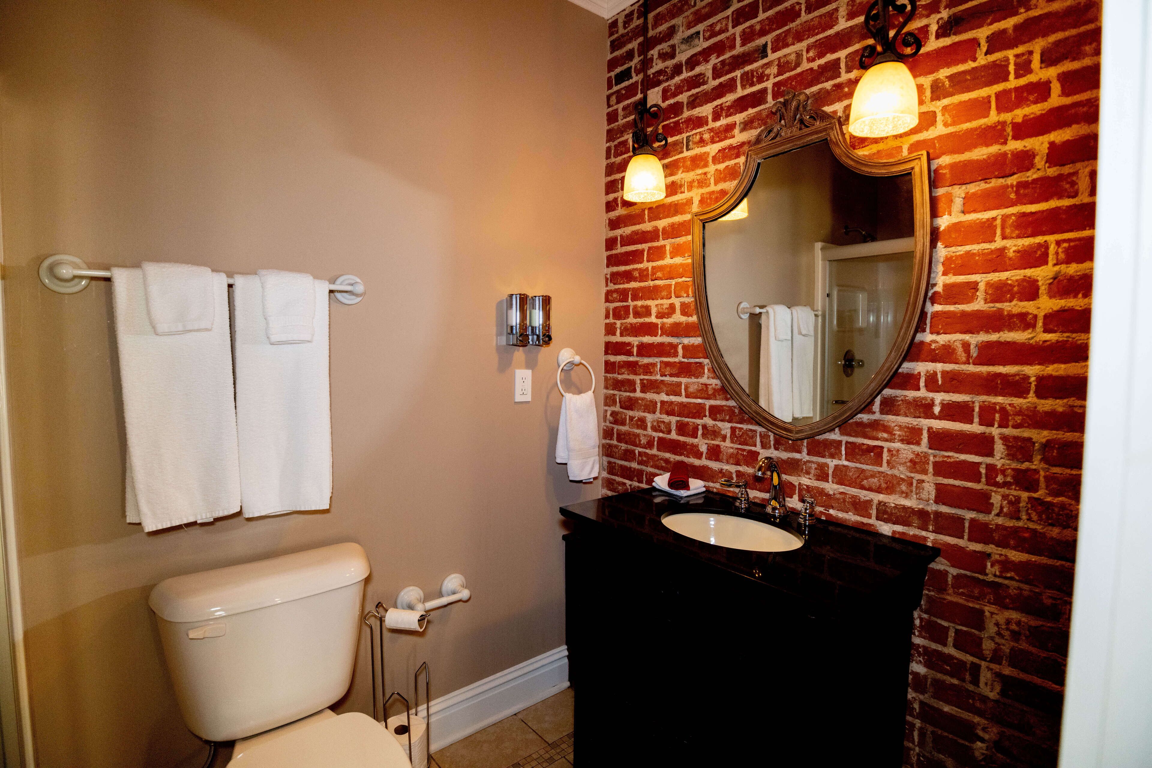 Een badkamer met toilet, wastafel en een spiegel aan een bakstenen muur.