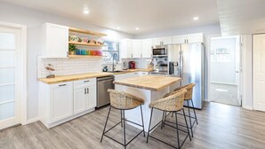 A modern kitchen with white cabinetry, a wooden countertop, and a central island with bar stools.