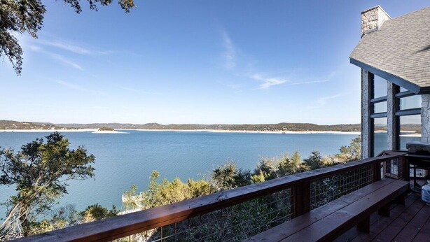 A wooden deck with a view of a calm lake and distant shoreline.