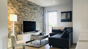 Een moderne woonkamer met een stenen muur, een flatscreen televisie, een bank, een salontafel en een lamp.