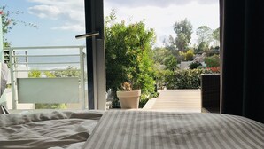 Een slaapkamer met een bed, uitzicht op een balkon en een potplant.