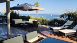 Een terras buiten met een zwembad, lounge fauteuils en een bank.
