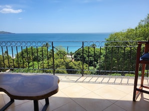 A balcony with a view of the sea, a wooden table, and a chair.