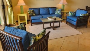 Un salon avec un canapé bleu, des fauteuils assortis, une table basse et deux lampes.
