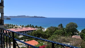 A coastal view from a balcony overlooking a beach, with buildings and palm trees in the foreground. - Ocean Views and Gorgeous Sunsets. 3 BR in Playa Flamingo! (Playa Flamingo)