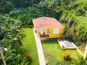 A small yellow building with a brown roof, surrounded by lush greenery and a well-maintained lawn. - Unique Casa and Casita Heliconia- 2 separate properties and salt water spa. (Naguabo)