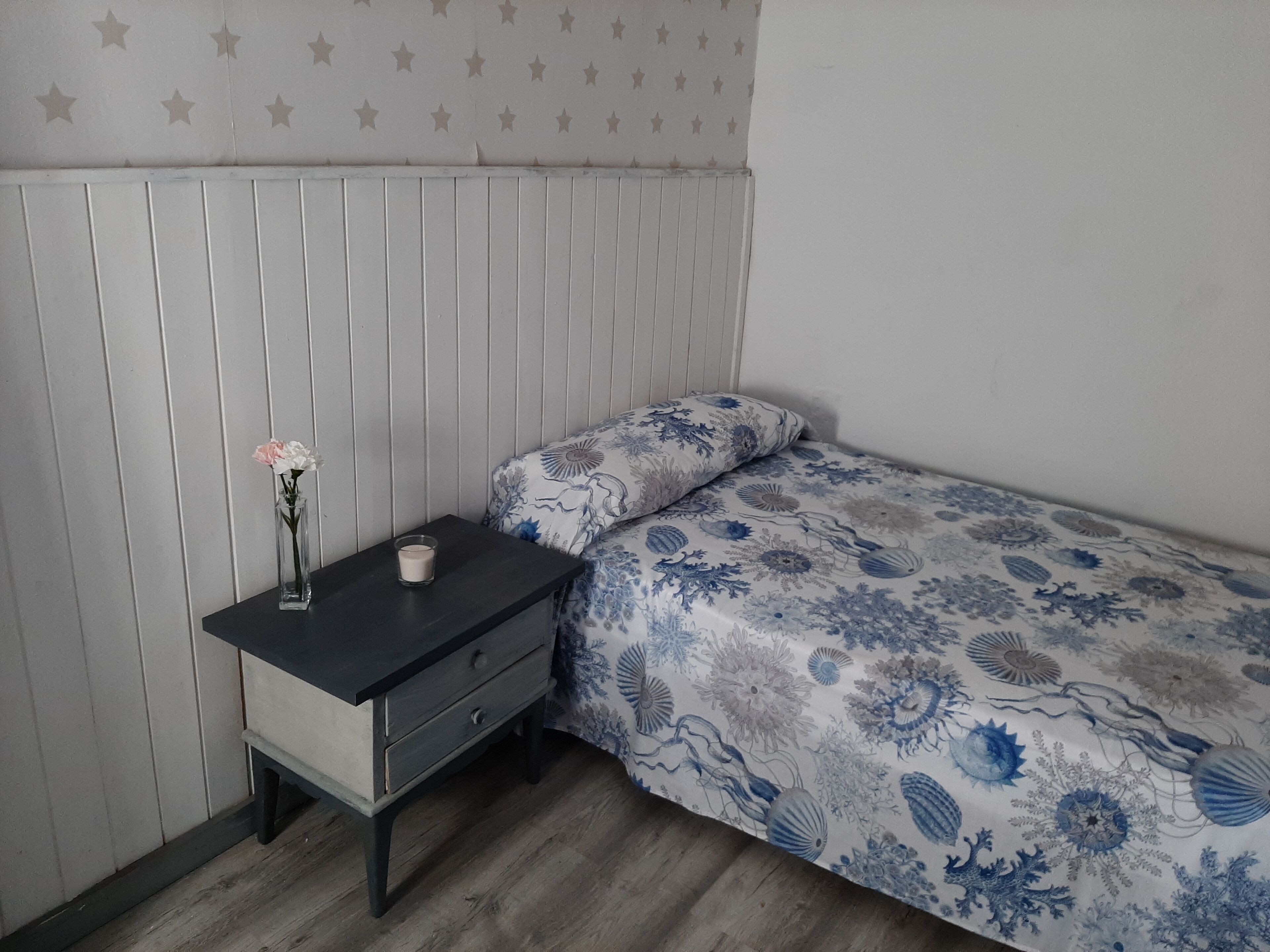 Un dormitorio con cama, mesita de noche, un florero con flores y una pared con diseño de estrellas.