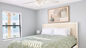 A bedroom with a bed, a ceiling fan, a window with blinds, and a painting on the wall. - Bright 2-bed, 1-bath condo in the heart of Indian Rocks Beach, just a 2-min walk to the sand and steps from local cafés & shops. Enjoy a shared POOL, private balcony, washer/dryer, free parking — ideal for couples, friends, families & pet-friendly! (Indian Rocks Beach)