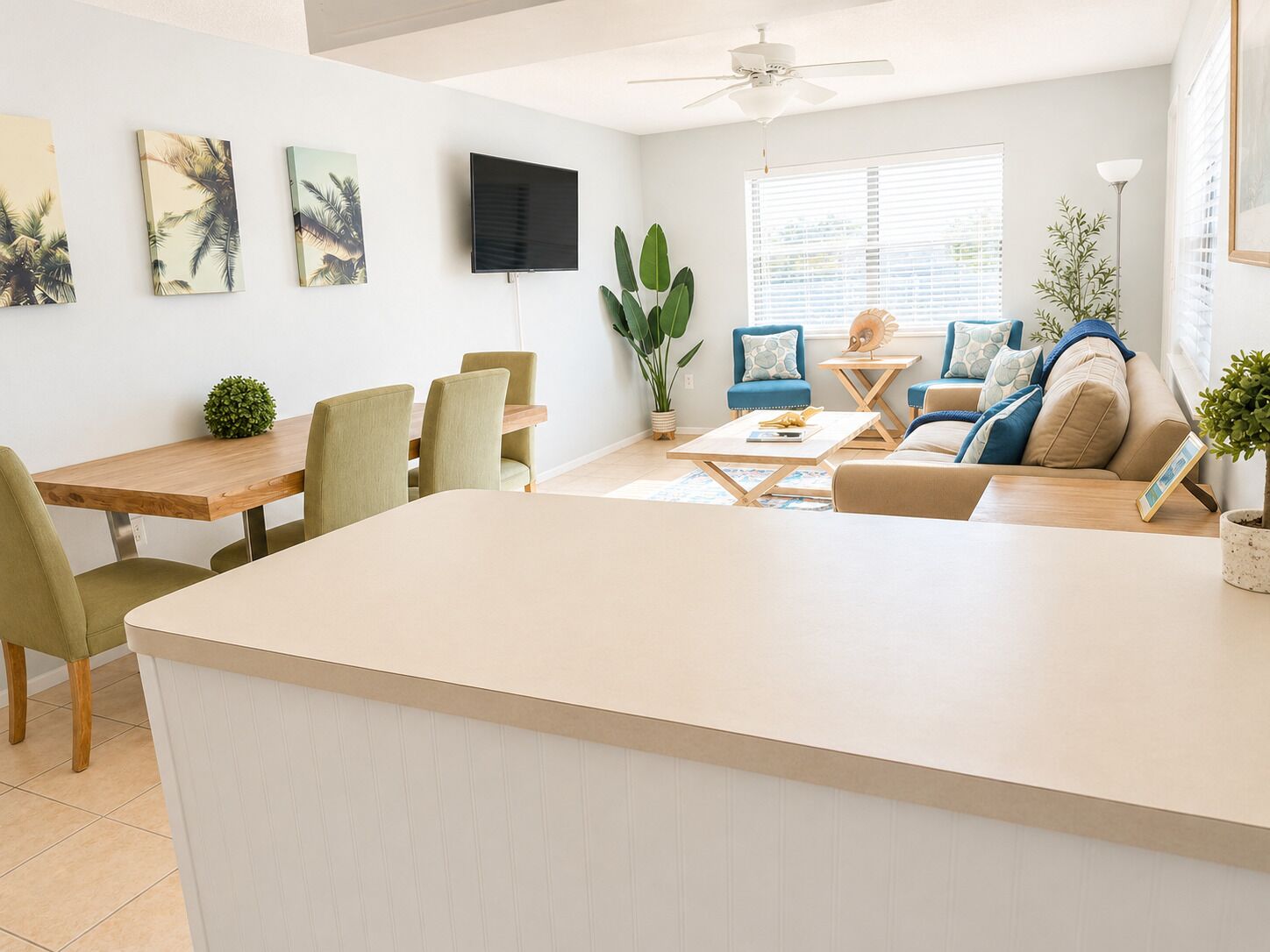 A modern living room with a dining area, a flat-screen TV mounted on the wall, and a ceiling fan.