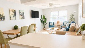 A modern living room with a dining area, a flat-screen TV mounted on the wall, and a ceiling fan. - Bright 2-bed, 1-bath condo in the heart of Indian Rocks Beach, just a 2-min walk to the sand and steps from local cafés & shops. Enjoy a shared POOL, private balcony, washer/dryer, free parking — ideal for couples, friends, families & pet-friendly! (Indian Rocks Beach)