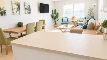 A modern living room with a dining area, a flat-screen TV mounted on the wall, and a ceiling fan.