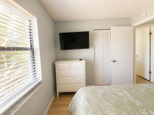 Une chambre à coucher avec un lit, une commode, un téléviseur et un placard.