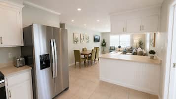 A modern kitchen with a stainless steel refrigerator, a dining area with a table and chairs, and a small island with a sink.
