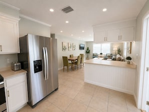A modern kitchen with a stainless steel refrigerator, a dining area with a table and chairs, and a small island with a sink.
